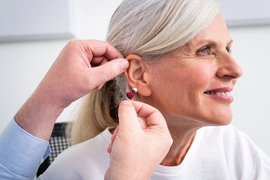 Eine Frau bekommt ein modernes Hörgerät eingesetzt und lächelt zufrieden.